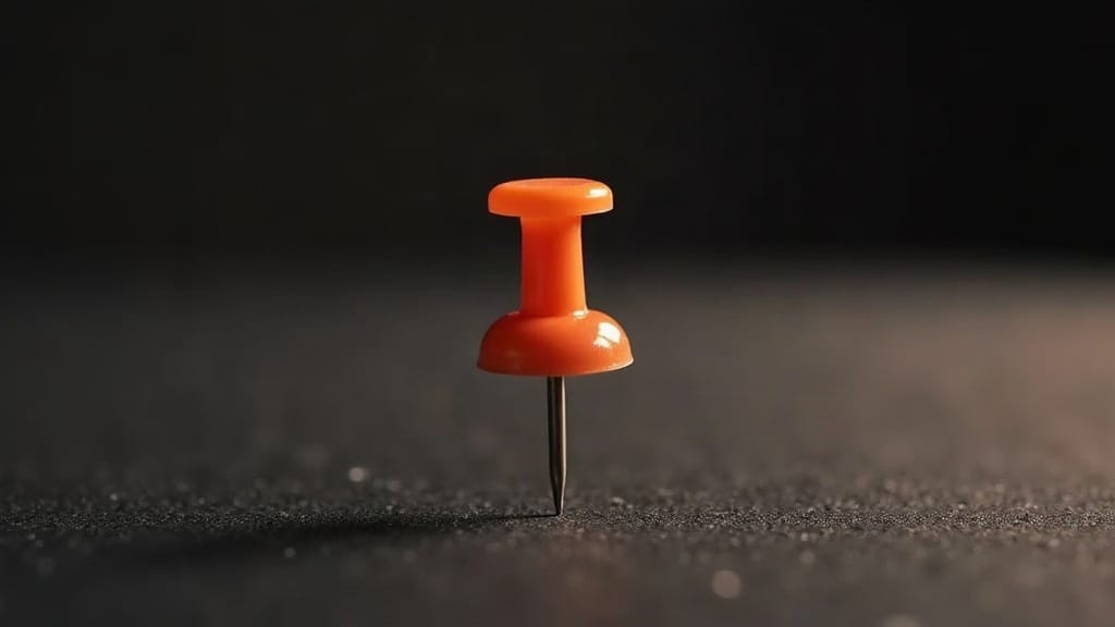 A single pushpin standing upright on a dark surface, sharp at center with tilt-shift depth of field blurring toward the edges, lit from the left with warm amber side-lighting.
